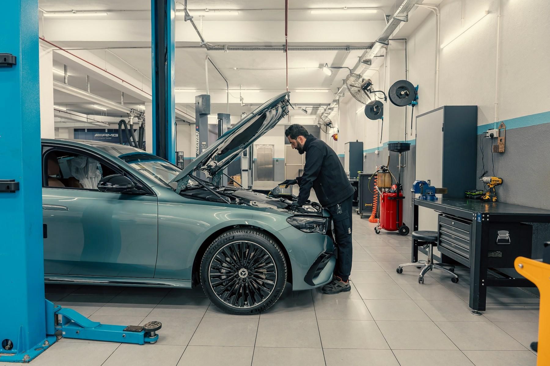 Mechanikas dirba prie automobilio pakeltu variklio dangčiu servise.
